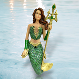 The Atlantica Ornament by December Diamonds showcases a mermaid with long brown hair in a green and gold scale outfit, holding a gemstone-adorned trident against a shimmering water backdrop, ideal for holiday decor and creating an enchanting aquatic scene.