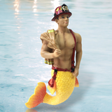 The Back Draft Ornament by December Diamonds features a merman with a muscular upper body and vibrant yellow fish tail, wearing a firefighters helmet and suspenders, confidently holding a hose against a water backdrop.