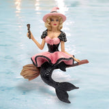 The Baywitched Ornament by December Diamonds is a whimsical holiday decor piece featuring a pink-dressed witch with a black mermaid tail and broomstick, set against a water-themed backdrop. An exquisite blend of whimsical charm, its reminiscent of mystical mermaid ornaments.