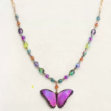 Introducing the Ultra Violet Bella Butterfly Beaded Necklace by Holly Yashi, featuring a striking purple butterfly pendant and a vibrant chain of multicolored beads in shades of purple, green, and orange—perfect for adding a splash of color to any plain background.