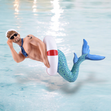 The Big Tube Ornament by December Diamonds features a Barbie-style merman with a muscular build, sunglasses, blue scarf, white sailor hat, green mermaid tail, and red-and-white float. Playfully posed on shimmering water, this figure serves as festive holiday decor or a Merman ornament.