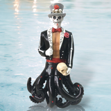 The Calavera Ornament by December Diamonds combines a mermans elegance and an octopuss mystique, featuring a black suit with a white collar, skull-adorned top hat, and a sugar skull face on light blue. It clutches another skull, making for an intriguing decoration.