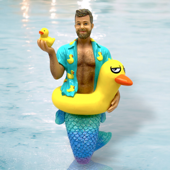 The Daddy Duckie Ornament by December Diamonds features a bearded merman with a green scale tail in a pool. Hes wearing a duck-patterned shirt, holding a rubber duck, and has a large yellow float. Perfect for whimsical holiday decor, hes ready to make waves in any setting!.