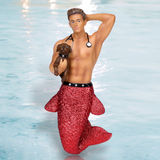 The Dr. Pet a Vet Ornament by December Diamonds features a doll with a red glitter mermaid tail and a stethoscope, posing confidently in water. It holds a small brown dog under one arm, with the other arm raised behind its head against a light blue background reminiscent of tranquil waters.