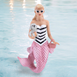 The Fifi Ornament from December Diamonds features a doll with a pink mermaid tail, black and white striped top, and sunglasses, holding a small dog and pink purse. Surrounded by ocean-themed details, she exudes aquatic charm.