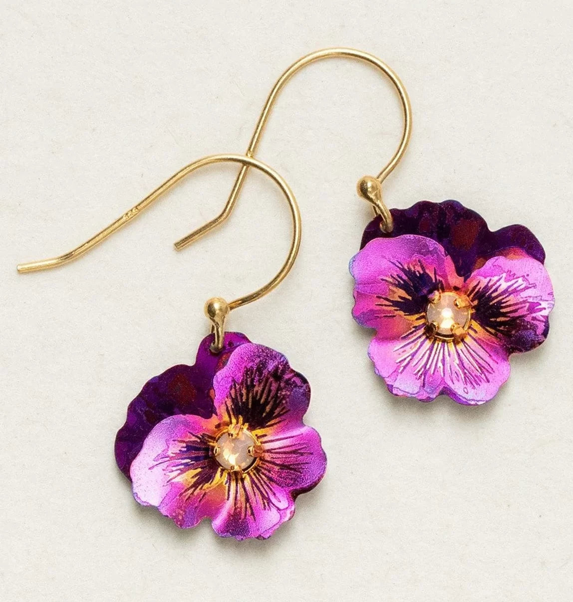 Explore Holly Yashis Sparkling Fuchsia Garden Pansy Drop Earrings featuring vibrant purple pansies with detailed petals and a sparkling center gem. These hypo-allergenic earrings blend artistry and comfort, set against a plain white background.