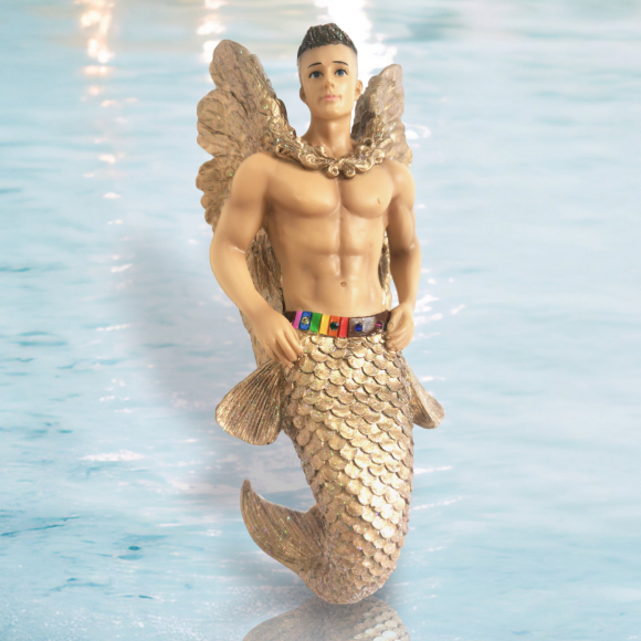 The Gaybriel Ornament by December Diamonds features a muscular, golden mermaid with wings against a blue water background. With its detailed scaled tail and colorful belt, its perfect holiday decor that adds a whimsical touch to any mermaid ornament collection.