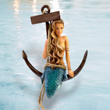 The Great Catch Ornament by December Diamonds features a mermaid with long blonde hair and a blue-scaled tail perched on an anchor wrapped in rope against a watery backdrop, seamlessly blending mythical and nautical themes. Its ideal for holiday decor or enhancing your mermaid collection.