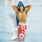 The Hung 10 Ornament by December Diamonds showcases a merman with a muscular upper body and a red and white floral tail. Hes posed with arms behind his head, casually leaning against a blue surfboard on a watery background, perfect for enhancing your holiday decor.