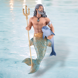 A merman from December Diamonds Hydros Ornament collection features long gray hair and intricate ornaments, holding a trident and dolphin. His golden-turquoise tail shimmers, adorned with a necklace against a light blue ocean backdrop.