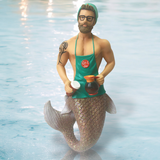 The Java Joe Ornament by December Diamonds features a bearded merman with glasses, a beanie, and apron, holding a coffee pot and cup. A tattoo is on his arm above his shimmering tail, set against calm waters. Perfect as holiday decor.