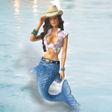 The hand-painted Jessie Ornament by December Diamonds features a mermaid with long hair, a cowboy hat, and tied shirt. Her sparkling blue tail against a watery backdrop, accessorized with bracelets and belt, makes her perfect for holiday decor or Merman and Mermaid collections.