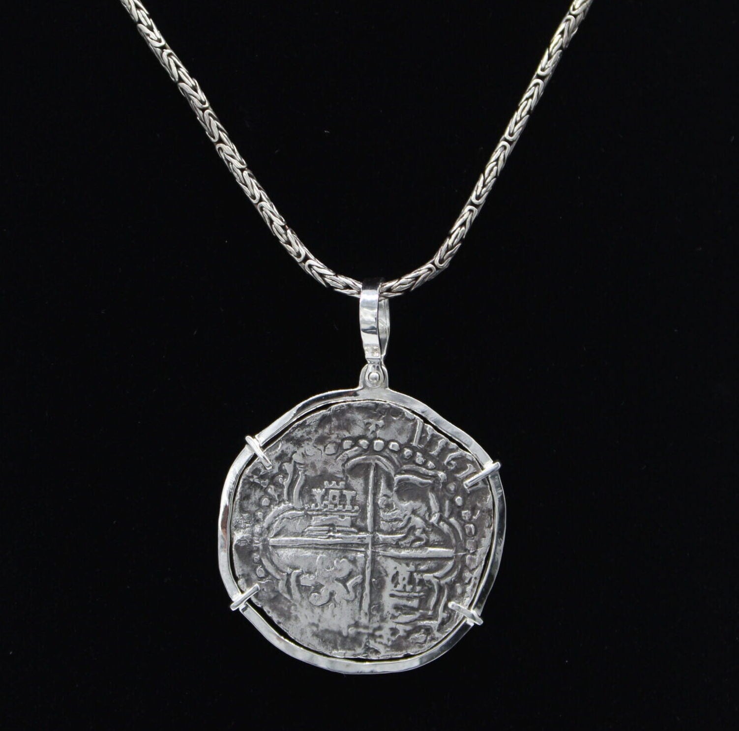 The Treasure Shoppe Inc.s Large Potosi Frame Coin pendant from Atocha Shipwreck Coins displays a large, round coin in a sterling silver bezel with intricate, worn details, reminiscent of the classic designs, suspended against a black background.