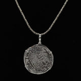 The Treasure Shoppe Inc. offers the Large Potosi Frame Coin, a pendant inspired by Atocha shipwreck coins. This intricate piece showcases a silver coin set in a sterling bezel against a solid black background, creating an exquisite design.