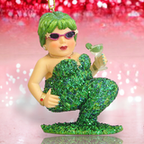 The Green Margarita Ornament by December Diamonds features a whimsical merman in a green sequined outfit, sunglasses, and holding a cocktail glass, with a glittery red and pink bokeh background.