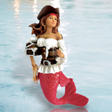 The Miss Bootylicious Ornament by December Diamonds showcases a mermaid with a shimmering pink tail, pirate hat, and off-shoulder top adorned with mermaid ornaments. She carries a treasure chest and gold chains, set against softly rippling blue water for a charming holiday decor scene.