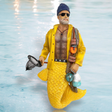 The Monty the Fisherman Ornament by December Diamonds is a unique merman with a yellow mermaid tail and raincoat, beanie, sunglasses, and gray beard. Holding a net and fishing gear, it reflects light softly, making it an ideal addition to your holiday decor.