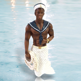 The Navy Soul Ornament by December Diamonds features a doll dressed as a sailor with a glittery white mermaid tail, anchor-themed hat, navy scarf, coiled rope, and gold wristwatch, standing in shallow water—ideal for mermaid enthusiasts.