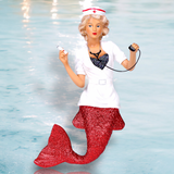 The Nurse Naughty Ornament by December Diamonds features a nurse-dressed mermaid with a red tail, white uniform, syringe, and stethoscope against a light blue aquatic backdrop, bringing an enchanting touch to any festive display.