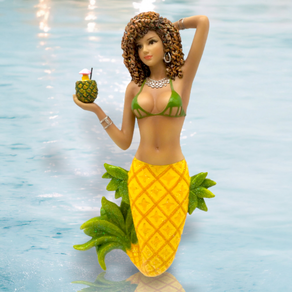 The Pina Ornament by December Diamonds is a hand-painted mermaid figurine ideal for holiday decor. It features curly brown hair, a green bikini top, and a yellow tail with green accents. She holds a pineapple-shaped drink with a straw and umbrella, set against shimmering blue waters.