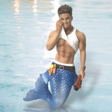 The Plumbers Crack Ornament by December Diamonds features a merman with short curly hair, a white sleeveless top, and a blue scale-patterned tail, holding a trident. Perfect for holiday décor, it stands out against a shimmering water surface backdrop.