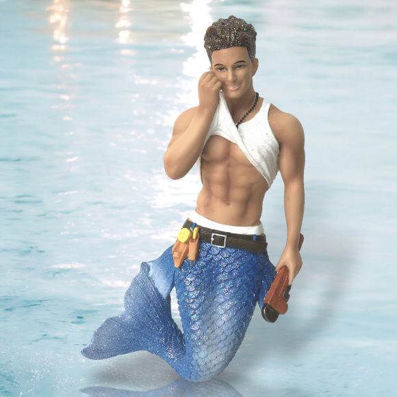 The Plumbers Crack Ornament by December Diamonds features a merman with short curly hair, a white sleeveless top, and a blue scale-patterned tail, holding a trident. Perfect for holiday décor, it stands out against a shimmering water surface backdrop.