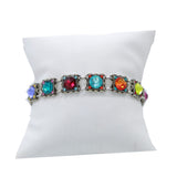 Fireflys Rainbow Square Multi Color Bracelet features vibrant square gemstones in blue, red, orange, green, and purple set in silver. Handmade in Guatemala and hypo-allergenic for all-day comfort, its showcased on a white cushioned stand.