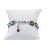 The Rainbow Square Multi Color Bracelet by Firefly is a beautiful handmade hypoallergenic piece from Guatemala, featuring multicolored square gemstones on a silver chain with a small red charm at the clasp, elegantly presented on a white cushion.