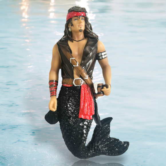 The Salvador Ornament by December Diamonds features a hand-painted merman pirate with long hair, a red headband, earrings, and a black vest holding a sword. His black glittering tail contrasts beautifully with the light blue water background—perfect for your holiday decor collection.