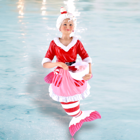 The Santas Head Baker Ornament from December Diamonds, part of the Merman and Mermaid collection, features a red and white-clad mermaid figure with a reflective tail, holding a candy cane-striped pink gift bag. A matching hat completes this festive decor piece.