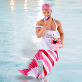 The Santas Taster Ornament by December Diamonds features a merman with pink hair, striped tail, and a Santa I Can Explain apron as he enjoys cupcakes. Its whimsical design is perfect for holiday decor against a watery backdrop.