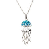Meet the Swarovski Crystals Aqua Jellyfish Necklace by Shanore: an exquisite ocean jewelry piece featuring a jellyfish pendant with turquoise gemstones. Crafted in sterling silver, its metallic tentacles dangle elegantly from a delicate chain against a plain white background.