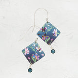 The Holly Yashi Garden Sonnet Blue Earrings showcase floral charm with square-shaped, nature-inspired pieces in blue and purple hues, accented by a round teal gemstone resting elegantly against a textured off-white background.