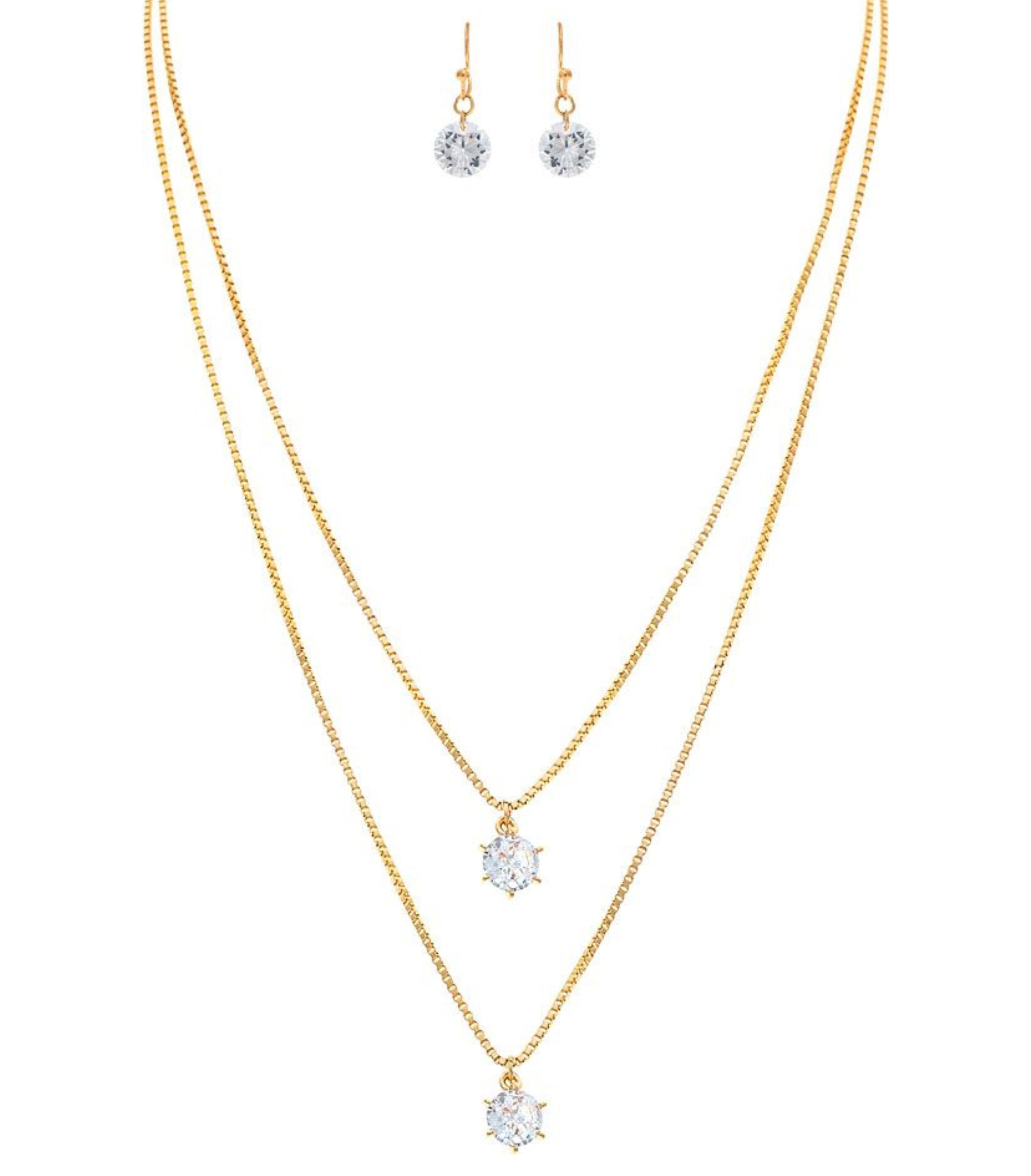 The A-Train Gold Double Chain Crystal Drop Necklace Set features a gold double chain and matching stud earrings with sparkling crystal drops, elegantly presented on a white background.