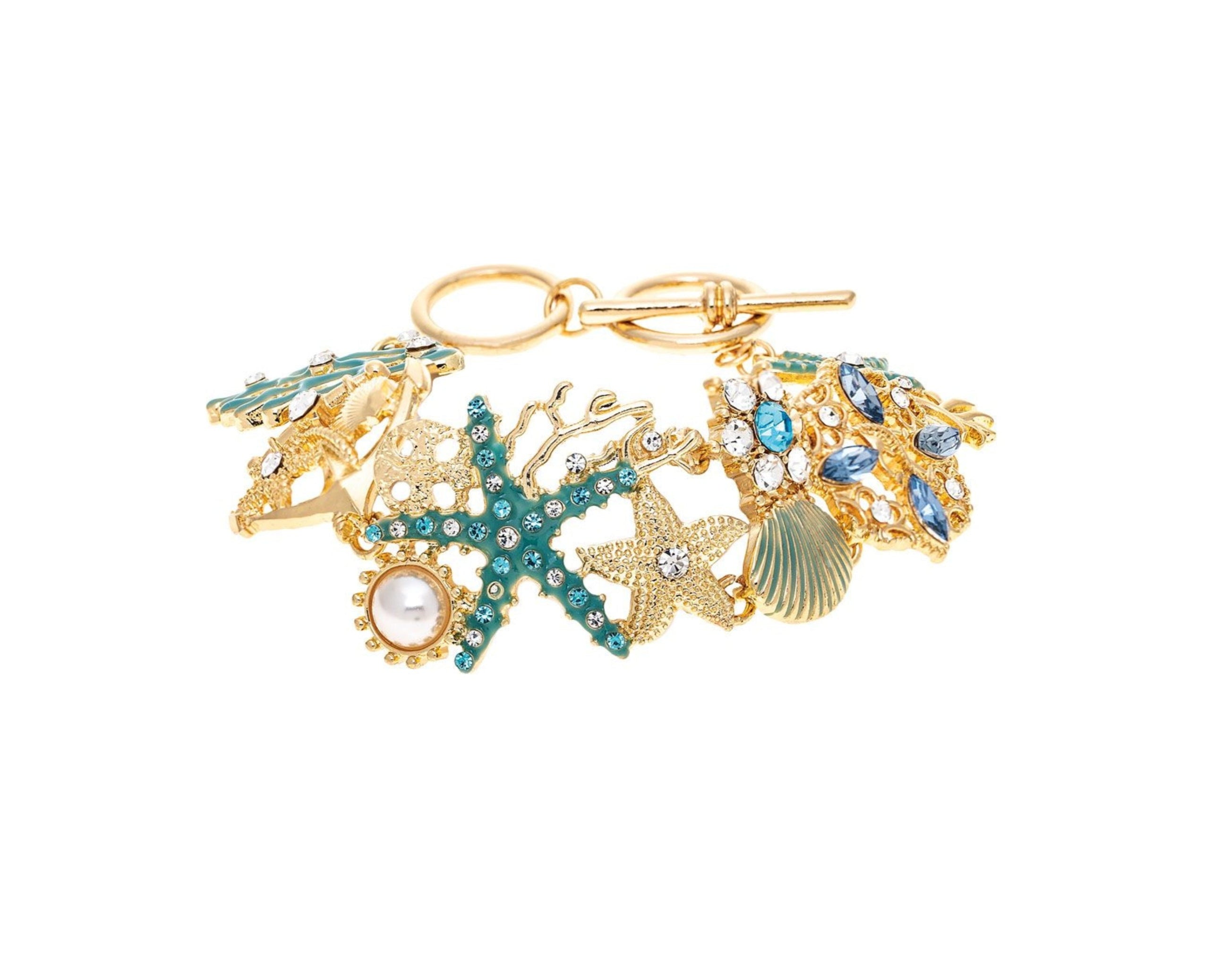 The A-Train Gold Enamel Crystal Seaside Mosaic Toggle Clasp Bracelet features sea-inspired charms—seashell, starfish, pearl, blue gemstones—set on white enamel and adorned with sparkling crystals.