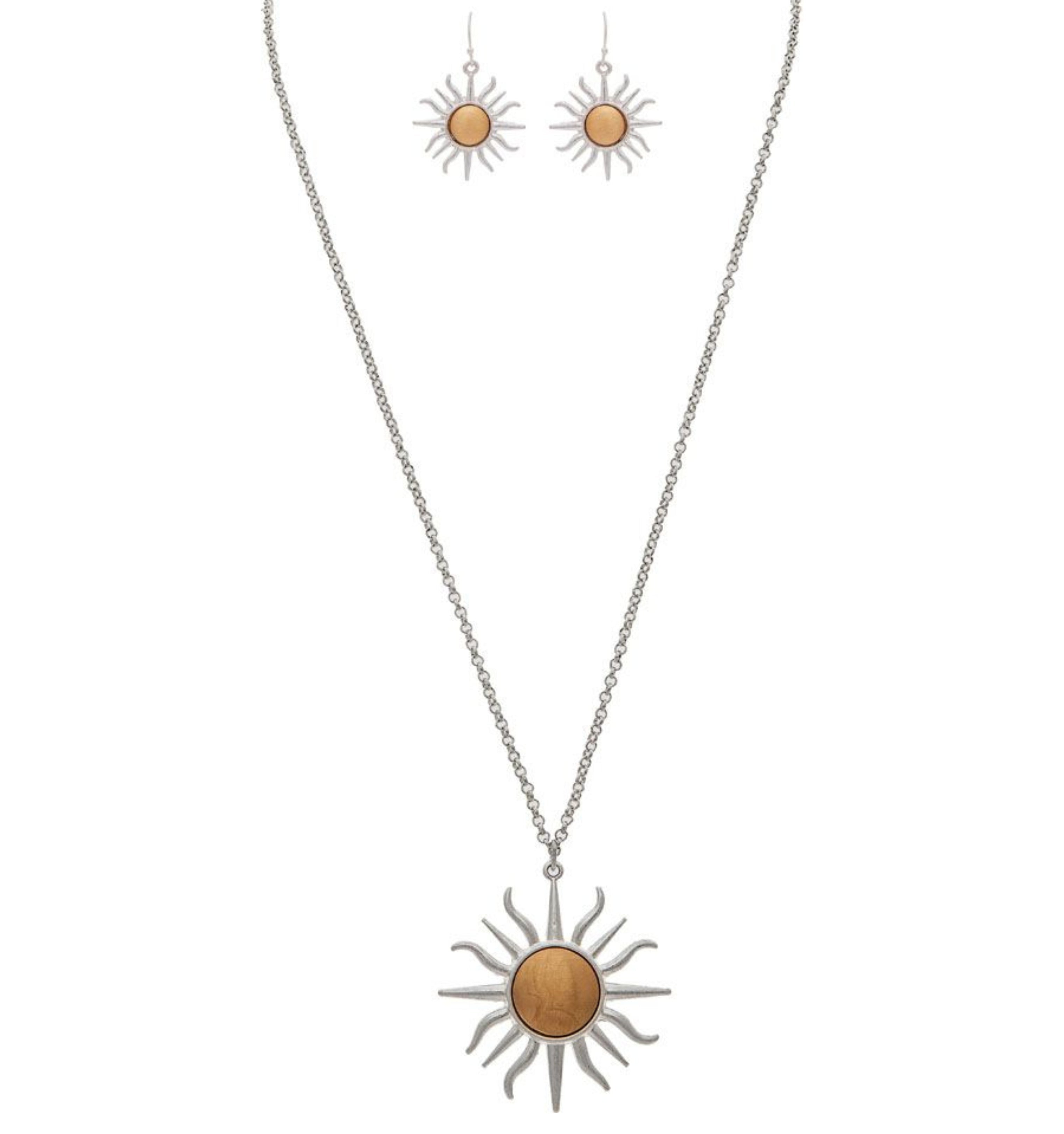 The A-Train Two-Tone Blazing Sun Necklace Set features sun-shaped pendants in mixed metals with gold-toned centers; the necklace boasts a bold sun pendant while the earrings display smaller matching designs.