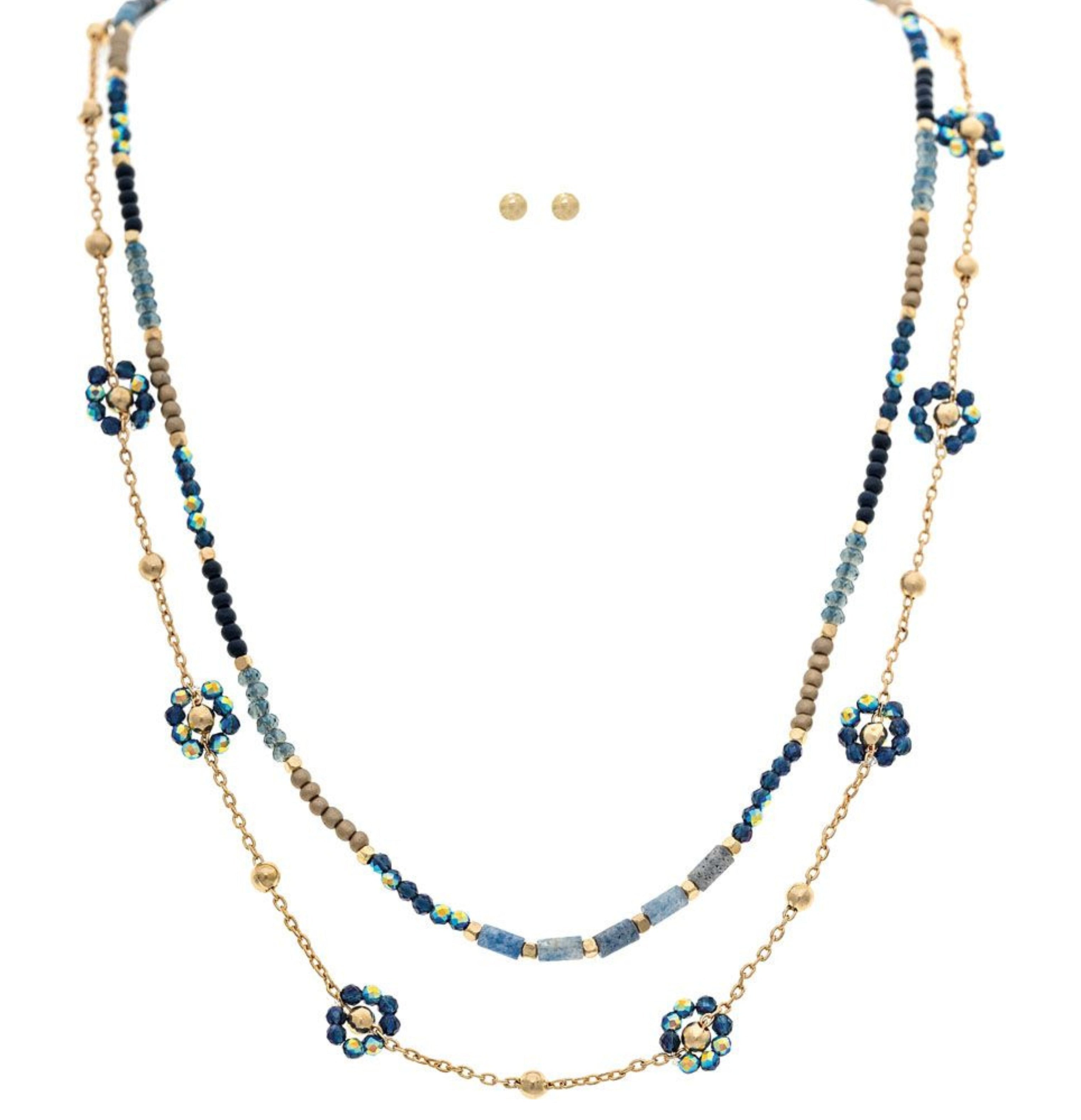 The A-Train Gold Blue Bead Layer Flowers Necklace Set features beige accents and flower-shaped clusters, paired with simple gold stud earrings for an elegant jewelry look, showcased on a white background.