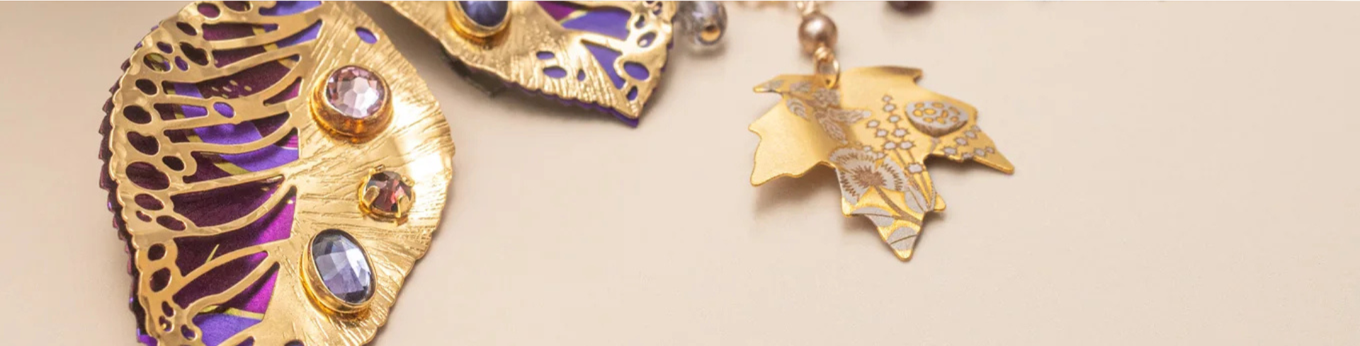 Gold chain necklace and matching earrings with square, colorful purple and blue enamel charms and gold accents, displayed alongside round, textured ornaments on a white surface.