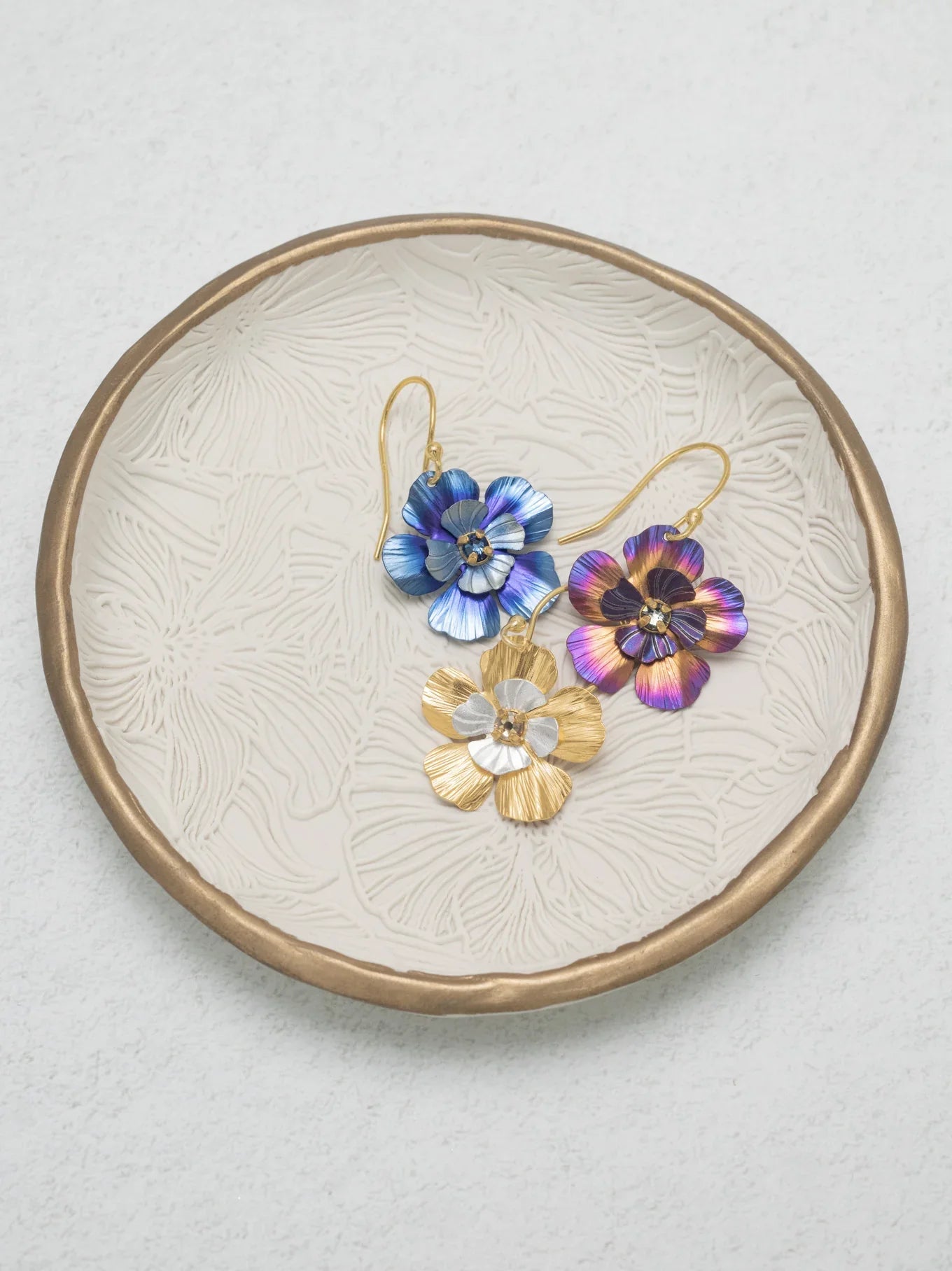 Gold chain necklace and matching earrings with square, colorful purple and blue enamel charms and gold accents, displayed alongside round, textured ornaments on a white surface.