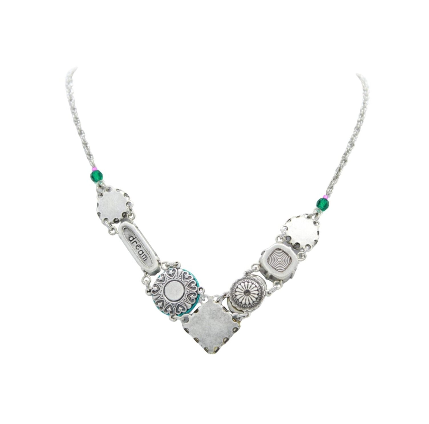 The La Dolce Vita “V” Emerald Necklace by Firefly is a handmade silver piece from Guatemala, featuring diverse pendants with intricate designs, including one inscribed with dream, and interspersed with green beads reminiscent of an emerald necklace.