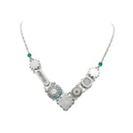 The La Dolce Vita “V” Emerald Necklace by Firefly is a handmade silver piece from Guatemala, featuring diverse pendants with intricate designs, including one inscribed with dream, and interspersed with green beads reminiscent of an emerald necklace.