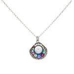 The Firefly Beach Pearl Large Shell Soft Necklace features a silver chain with a fan-shaped pendant, a central white stone, and colorful gems. Handmade in Guatemala, this fair-trade piece is set against a white background.