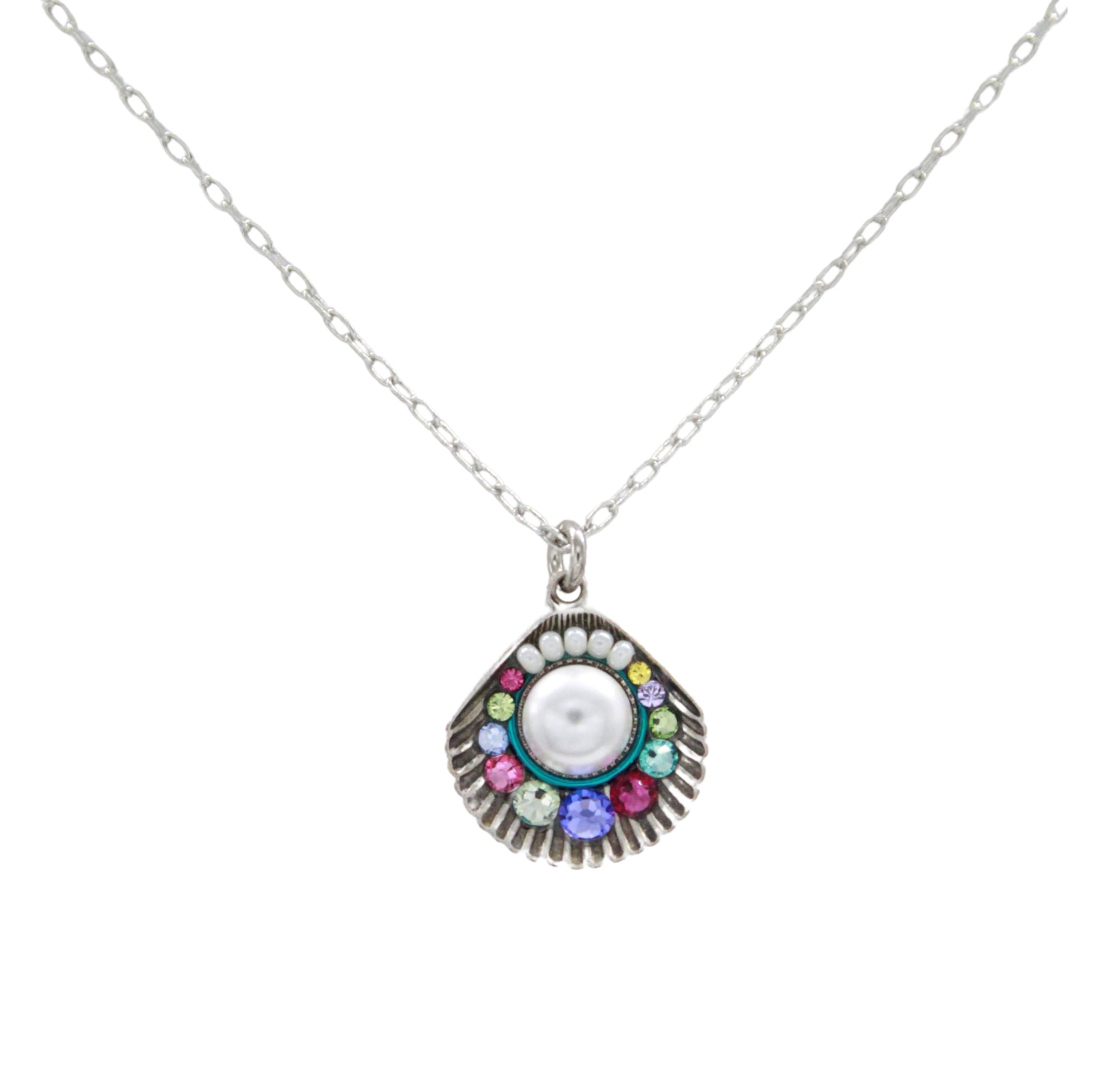 The Firefly Beach Pearl Large Shell Soft Necklace features a silver chain with a fan-shaped pendant, a central white stone, and colorful gems. Handmade in Guatemala, this fair-trade piece is set against a white background.