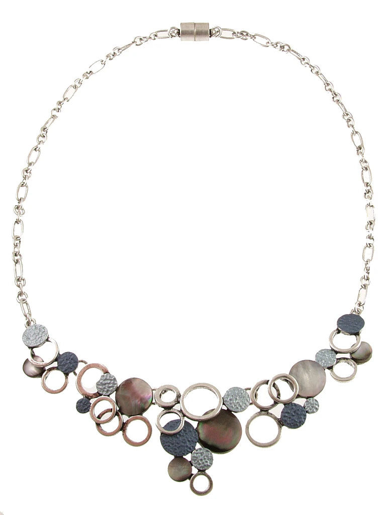 The Oxidized Silver/Blue & Black Lip Shell Necklace Set features an asymmetrical cluster of circular charms made of textured oxidized silver and iridescent lip shells.