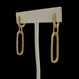The Be-Je Designs Gold Pave CZ Double Link Earrings feature handcrafted 14kt gold elongated oval links, some adorned with sparkling cubic zirconia, displayed on a simple gray stand against a black background.