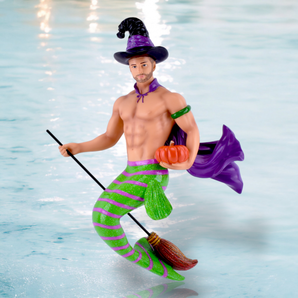 Renegade is a male merman ornament with a green and purple striped tail, wearing a purple witch hat and cape, flying on a broomstick while holding a small orange pumpkin.