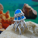 The Caribbean Opal Jellyfish-Pendant ONLY by Jewelry Network features a silver jellyfish design with blue synthetic opal inlays, displayed on a seashell with shimmering accents from softly blurred rocks and water in the background.