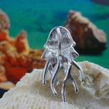 The Caribbean Opal Jellyfish-Pendant ONLY by Jewelry Network, crafted in 925 Sterling Silver with curved tentacles and a rhodium plate finish, rests on a textured white rock before a vibrant blue and orange seaside backdrop.