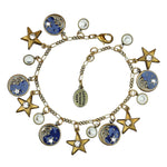 The Moon & Stars Charms Enamel & Stone Bracelet by Anne Koplik Designs, Inc. features gold star, moon, and round charms with white and blue accents—some crystal-embellished, others depicting a shimmering night sky scene.
