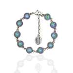 The Simple Drops Pacific Opal Bracelet by Anne Koplik Designs, Inc. features round iridescent stones in decorative bezels, link connections, an adjustable chain, and a small oval tag with engraved text.